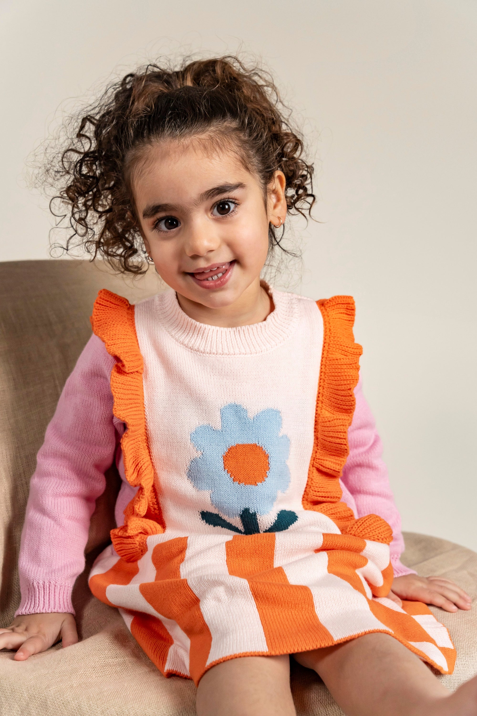 Toddler wearing Petal Playtime Cotton Knitted Dress with pink sleeves, orange ruffles, and a blue flower design. Cozy, soft cotton material, perfect for casual fall/winter outfits for toddlers.