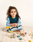 Toddler sitting and playing while wearing the Cloudy Daydream Cotton Knitted Sweater Dress, featuring blue sleeves, cloud patterns, and yellow tulips. Soft and cozy cotton, perfect for cooler seasons.