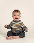 Baby wearing a cozy Fair Isle Sweater Jumper in dark grey with white and orange geometric patterns. Soft cotton, long-sleeved sweater perfect for keeping babies warm during fall and winter.