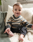 Baby wearing a cozy Fair Isle Sweater Jumper in dark grey with white and orange geometric patterns. Long-sleeved, soft cotton perfect for keeping toddlers warm during fall and winter. Ideal for casual wear.