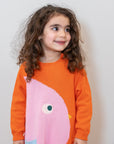 Toddler girl wearing Chirpy Bird Cotton Knitted Sweater Dress in bright orange with a pink bird design and pocket. Cozy, long-sleeve, soft cotton dress perfect for fall and winter. Ideal for playful outfits.