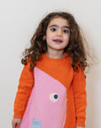 Toddler wearing a Chirpy Bird Cotton Knitted Sweater Dress in orange with a pink bird design and front pocket. Soft, long-sleeved, cozy cotton fabric perfect for fall and winter. Ideal for casual outings.