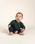 Adorable baby wearing a forest green Waffle Cotton Knit Jumper with yellow and white striped accents on the pocket, cuffs, and hem. Perfect for cozy warmth and style, ideal for everyday wear and playtime.