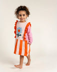 Toddler wearing Petal Playtime Cotton Knitted Dress featuring pink sleeves, orange ruffles, and stripes with a blue flower design. Soft, cozy, long-sleeved dress ideal for fall/winter casual wear.