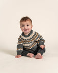 Baby wearing a Fair Isle Sweater Jumper in dark grey with white and orange geometric patterns. Cozy, long-sleeved, soft cotton ideal for keeping toddlers warm during fall and winter. Perfect for casual outfits.